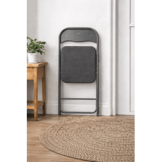 Chaise pliante grise pliée contre un mur, format compact pour rangement